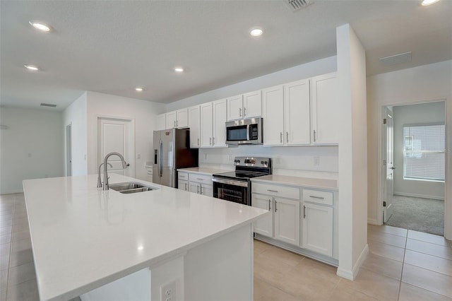 kitchen featuring sink, white cabinets, appliances with stainless steel finishes, a center island with sink, and light tile flooring