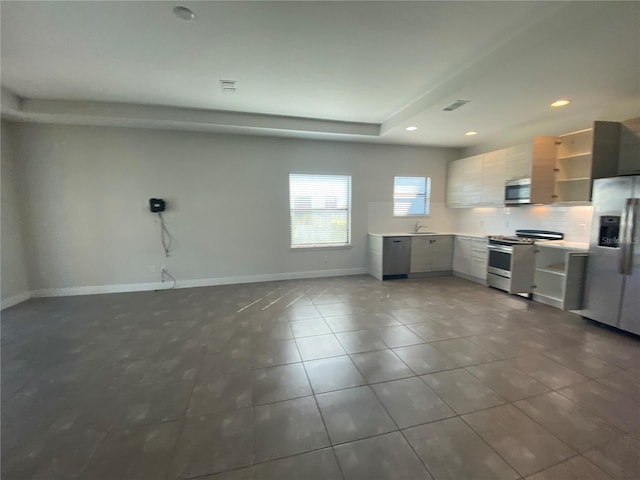 kitchen featuring dark tile flooring, tasteful backsplash, stainless steel appliances, and white cabinets