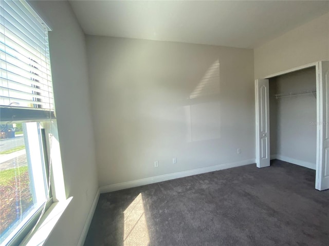 unfurnished bedroom featuring a closet, multiple windows, and dark colored carpet