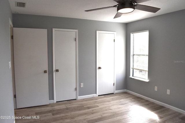 unfurnished bedroom featuring ceiling fan, light hardwood / wood-style flooring, and multiple closets