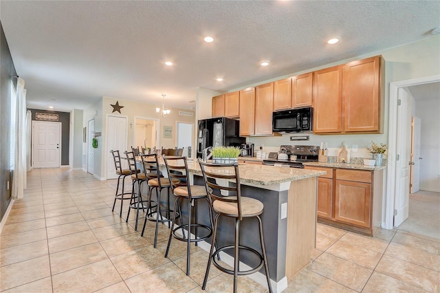 kitchen featuring light tile floors, black appliances, a kitchen breakfast bar, an island with sink, and light stone counters