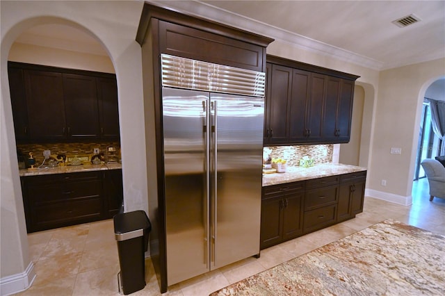 kitchen featuring dark brown cabinets, light stone countertops, stainless steel built in fridge, tasteful backsplash, and light tile floors