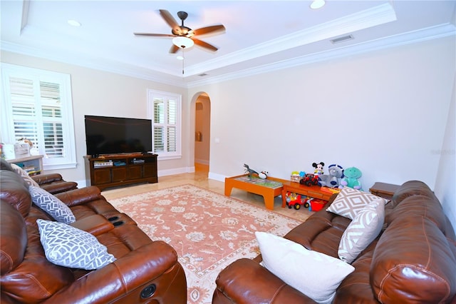 living room with a raised ceiling, ceiling fan, crown molding, and light tile flooring