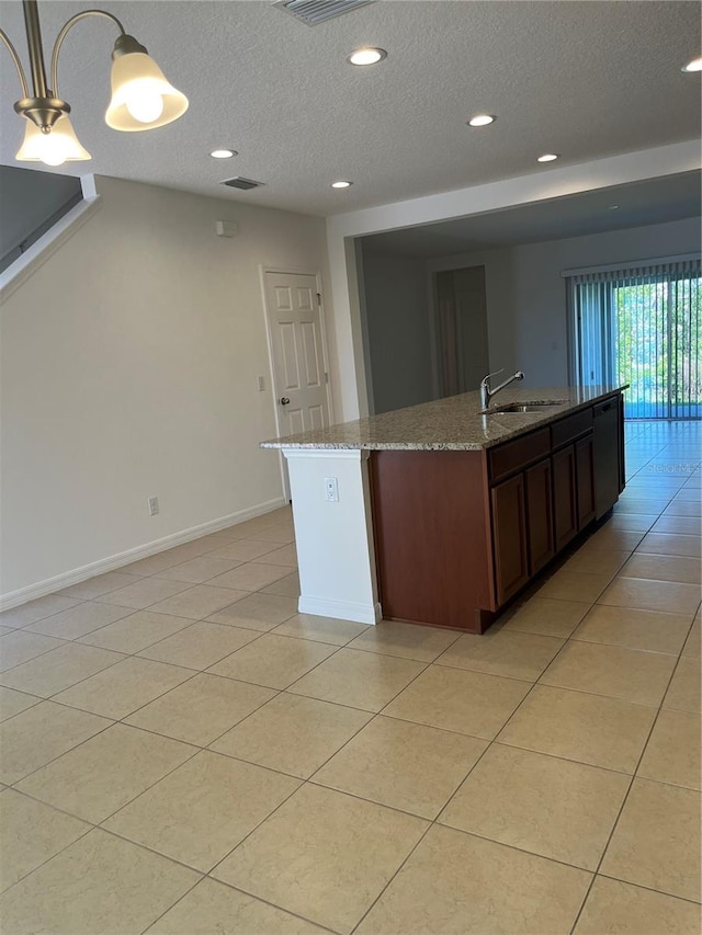 kitchen with light stone countertops, decorative light fixtures, light tile floors, a center island with sink, and a textured ceiling