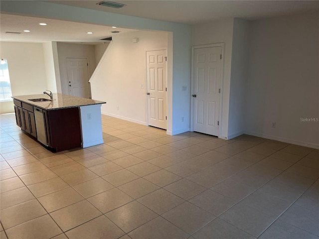 kitchen with light tile floors, dark brown cabinets, light stone counters, and sink