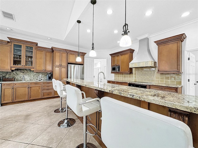 kitchen featuring backsplash, custom range hood, stainless steel appliances, crown molding, and decorative light fixtures