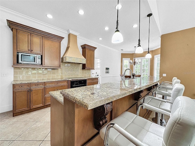 kitchen featuring a breakfast bar, stainless steel microwave, custom range hood, and hanging light fixtures