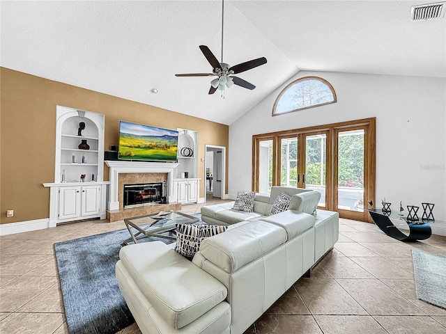 tiled living room with ceiling fan, french doors, built in features, high vaulted ceiling, and a fireplace