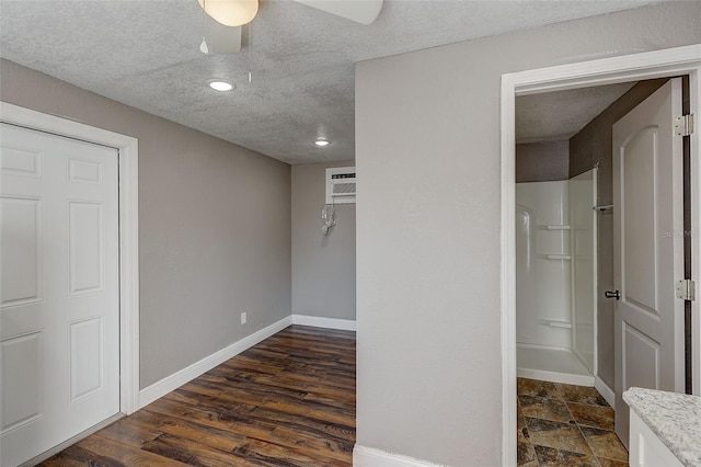 unfurnished bedroom featuring a wall mounted air conditioner, a textured ceiling, dark hardwood / wood-style flooring, ceiling fan, and a closet