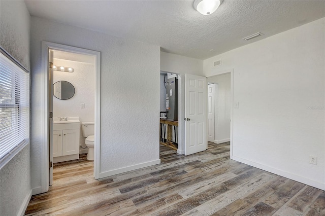 unfurnished bedroom with a textured ceiling, connected bathroom, sink, and hardwood / wood-style flooring