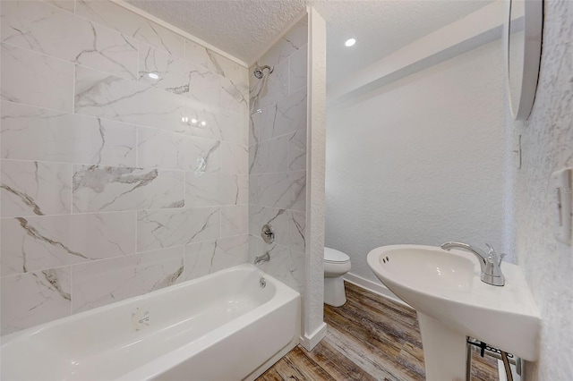 bathroom with hardwood / wood-style floors, toilet, tiled shower / bath combo, and a textured ceiling