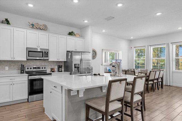 kitchen with white cabinetry, a kitchen island with sink, a breakfast bar, stainless steel appliances, and tasteful backsplash