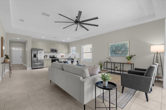 tiled living room featuring ceiling fan and a tray ceiling