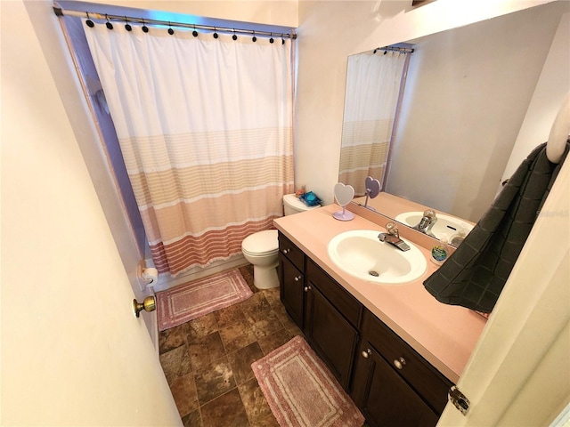 full bath featuring stone finish flooring, vanity, and toilet