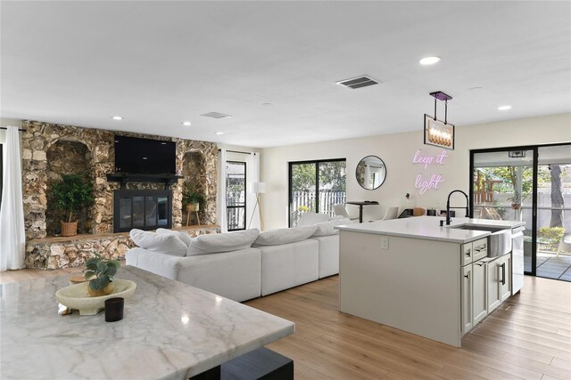 kitchen with decorative light fixtures, white cabinets, an island with sink, a wealth of natural light, and a stone fireplace