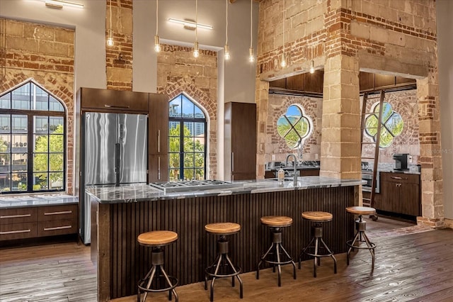 bar featuring dark brown cabinets, hardwood / wood-style floors, stainless steel appliances, and a high ceiling