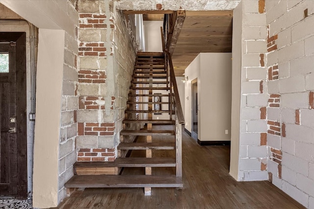 stairs featuring brick wall and dark hardwood / wood-style floors