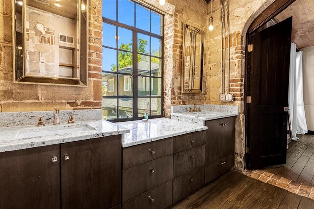 bathroom featuring hardwood / wood-style floors, dual sinks, brick wall, and vanity with extensive cabinet space