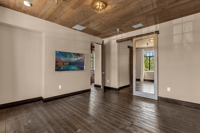 empty room featuring a barn door, dark wood-type flooring, and wooden ceiling