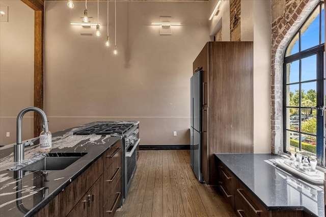 kitchen featuring hanging light fixtures, dark hardwood / wood-style flooring, sink, high quality appliances, and dark stone countertops