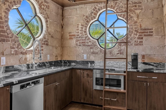 kitchen featuring wood-type flooring, brick wall, appliances with stainless steel finishes, sink, and dark stone counters