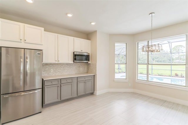 kitchen featuring baseboards, gray cabinetry, stainless steel appliances, light countertops, and tasteful backsplash