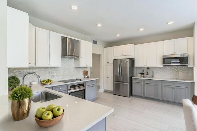kitchen with gray cabinetry, a sink, wall chimney range hood, appliances with stainless steel finishes, and light countertops