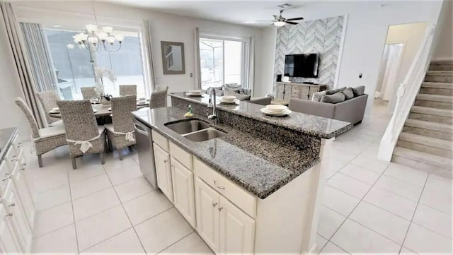 kitchen featuring light tile floors, dark stone countertops, sink, an island with sink, and ceiling fan with notable chandelier