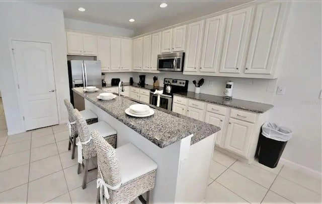 kitchen with light tile floors, appliances with stainless steel finishes, a kitchen bar, dark stone counters, and white cabinetry