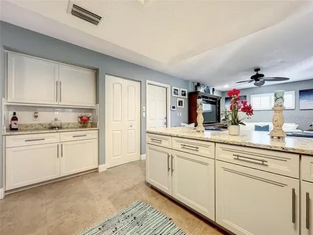 kitchen featuring light stone counters, white cabinets, visible vents, and a ceiling fan