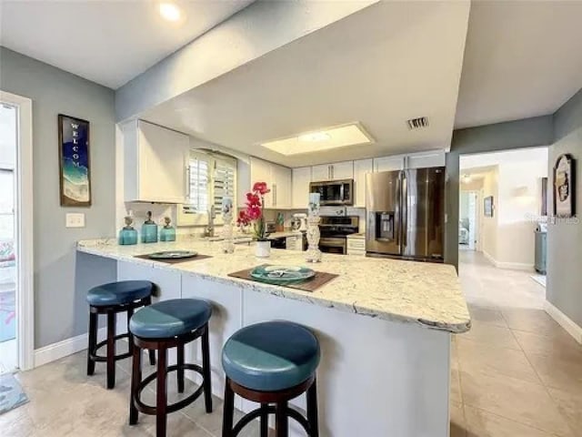 kitchen with light stone counters, a breakfast bar area, stainless steel appliances, a peninsula, and visible vents