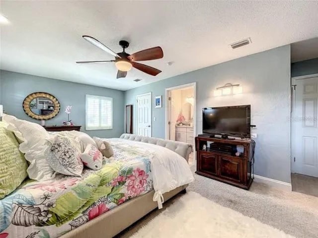 carpeted bedroom with visible vents, baseboards, ceiling fan, ensuite bathroom, and a textured ceiling