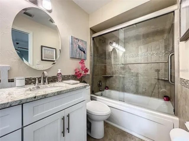 bathroom featuring combined bath / shower with glass door, visible vents, toilet, and vanity