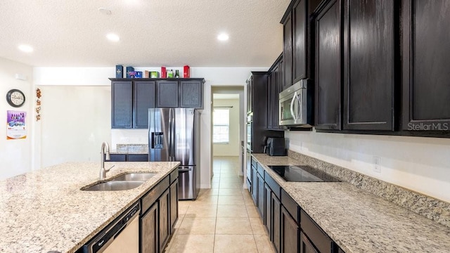 kitchen with a textured ceiling, light stone counters, sink, and appliances with stainless steel finishes