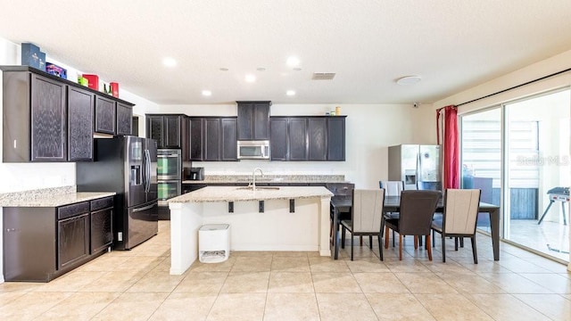 kitchen with a breakfast bar, sink, an island with sink, appliances with stainless steel finishes, and light stone counters