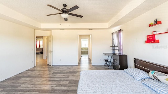 bedroom with hardwood / wood-style floors, ceiling fan, a raised ceiling, and a textured ceiling