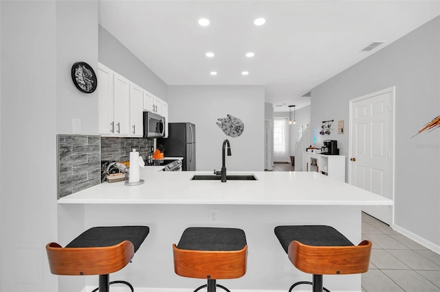 kitchen featuring a breakfast bar area, white cabinetry, stainless steel appliances, backsplash, and sink