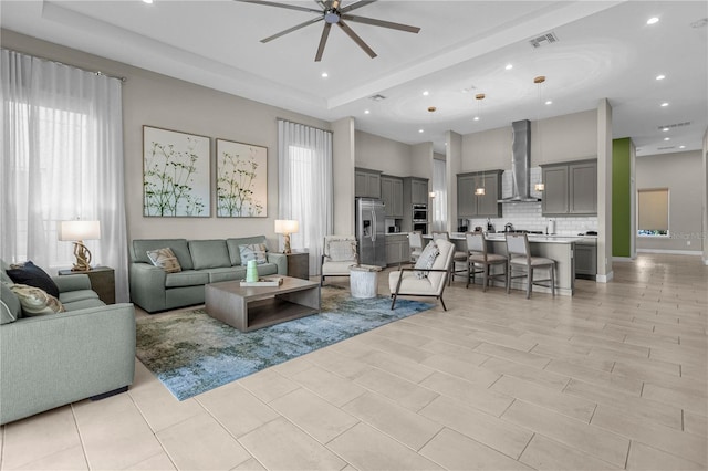 tiled living room with ceiling fan, a tray ceiling, and a wealth of natural light