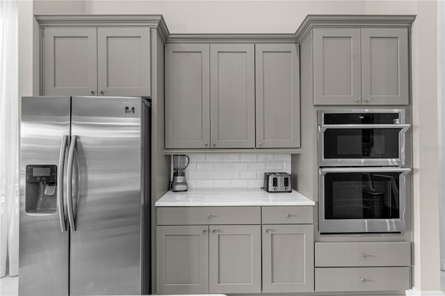 kitchen with gray cabinetry, stainless steel appliances, tasteful backsplash, and light stone countertops