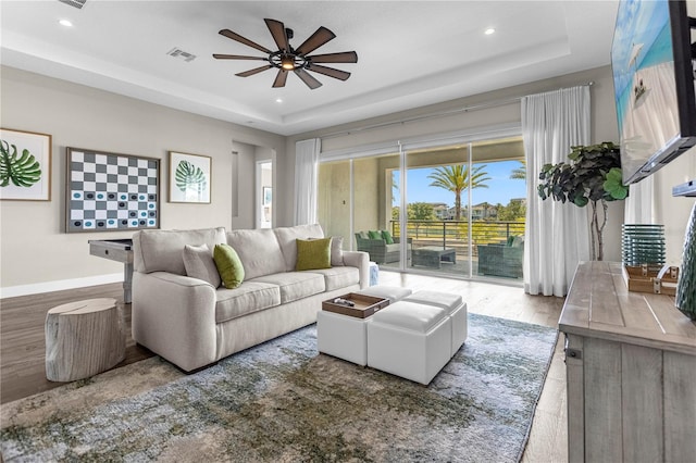 living room featuring a raised ceiling, ceiling fan, and hardwood / wood-style flooring