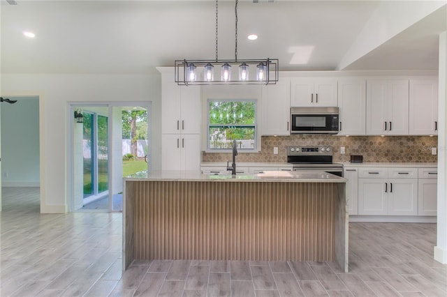 kitchen with white cabinetry, appliances with stainless steel finishes, pendant lighting, an island with sink, and lofted ceiling