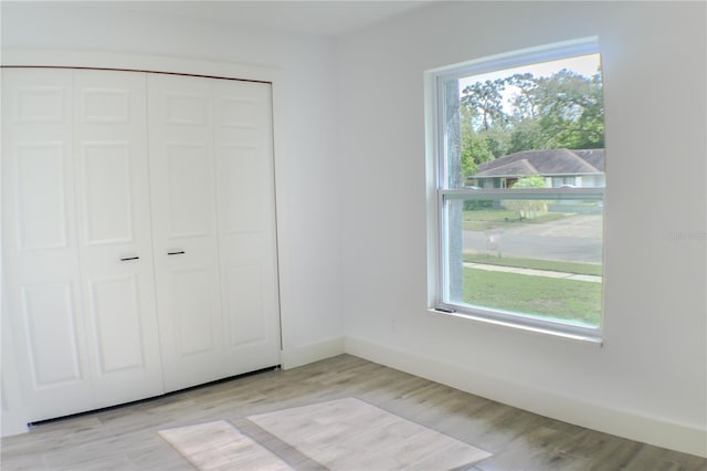 unfurnished bedroom featuring a closet, light wood-type flooring, and multiple windows