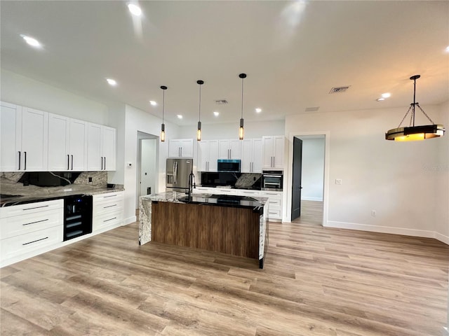 kitchen featuring tasteful backsplash, appliances with stainless steel finishes, decorative light fixtures, and a center island with sink