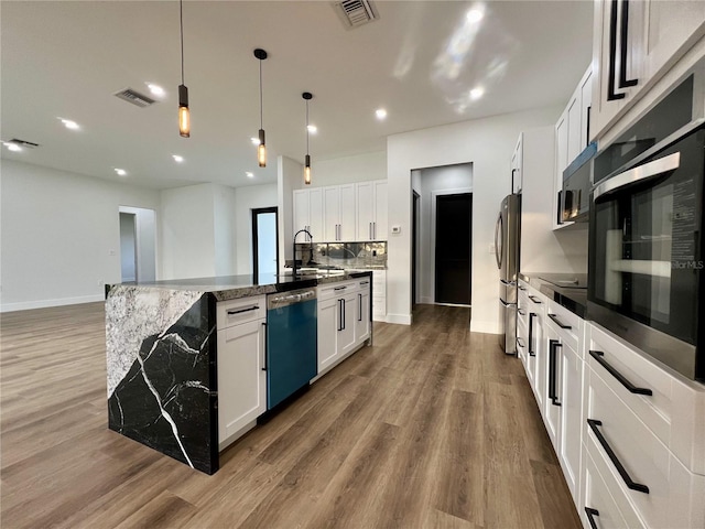 kitchen with white cabinetry, hardwood / wood-style floors, stainless steel appliances, a center island with sink, and pendant lighting