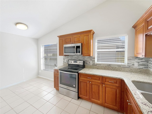 kitchen with appliances with stainless steel finishes, tasteful backsplash, vaulted ceiling, light tile floors, and light stone countertops