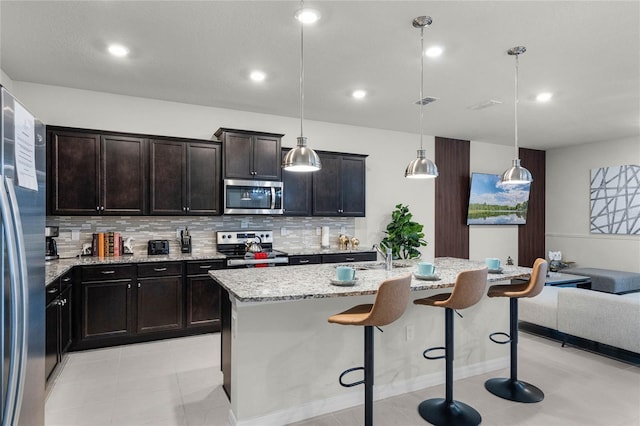 kitchen with hanging light fixtures, appliances with stainless steel finishes, light tile floors, a breakfast bar area, and tasteful backsplash