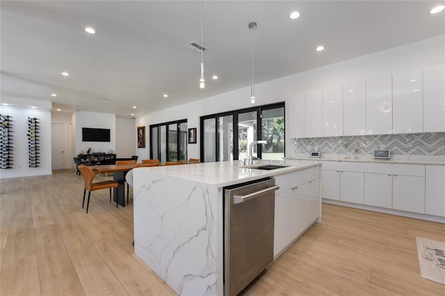 kitchen with white cabinets, an island with sink, light stone countertops, dishwasher, and sink