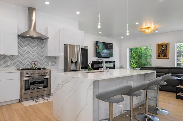 kitchen featuring appliances with stainless steel finishes, tasteful backsplash, white cabinets, light stone countertops, and wall chimney exhaust hood