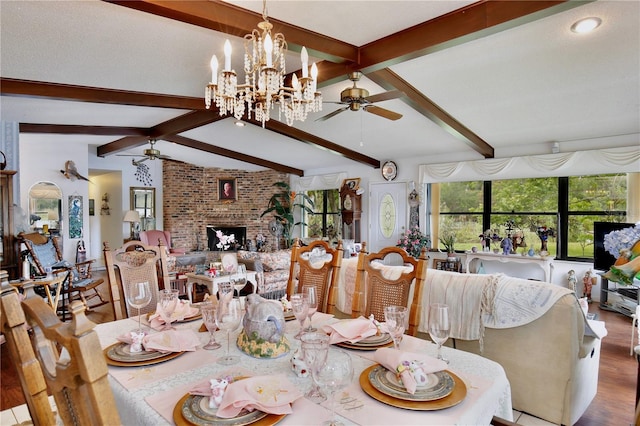 dining room with a brick fireplace, vaulted ceiling with beams, ceiling fan with notable chandelier, brick wall, and light hardwood / wood-style flooring