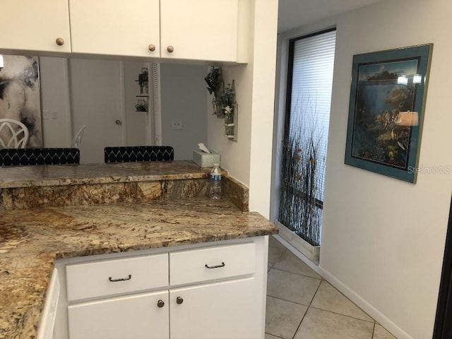 kitchen featuring kitchen peninsula, stone counters, white cabinetry, and light tile flooring